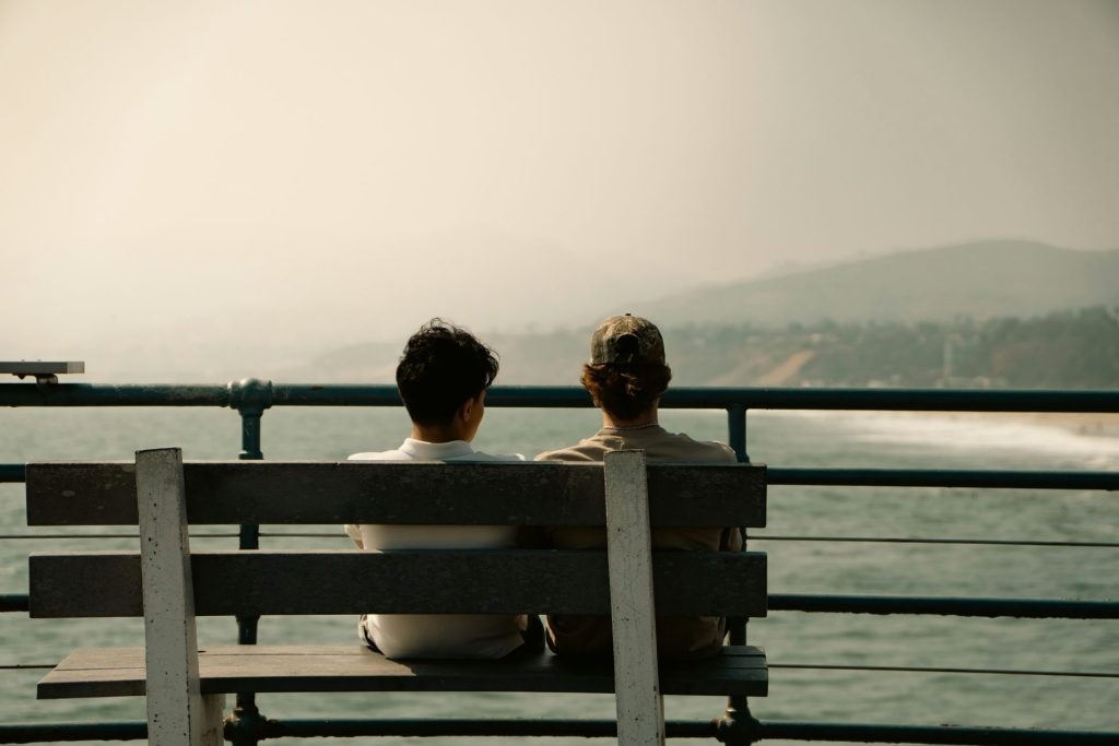 Two people sit on a bench overlooking the ocean.